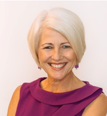 A silver-haired woman in a purple sleeveless shirt smiling at the camera